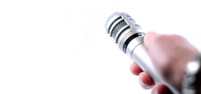 Main tenant un microphone argenté sur fond blanc, ambiance minimaliste et professionnelle